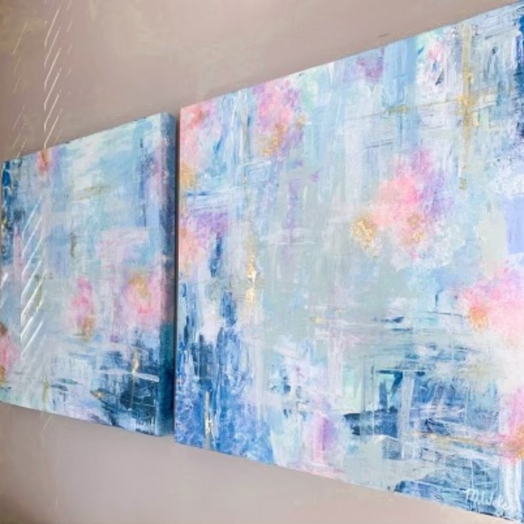 Two large canvas paintings are hanging on a tan wall and viewed from the side. The paintings are abstract mixes of color, featuring dark and light blues as well as subtle touches of pink, orange, and green.