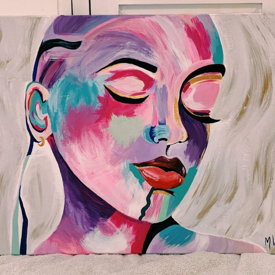 A abstract canvas painting of a women's face in bright purples, pinks, and blues with little gold details on her eyebrows and earrings. She is looking down, with her eyes closed.